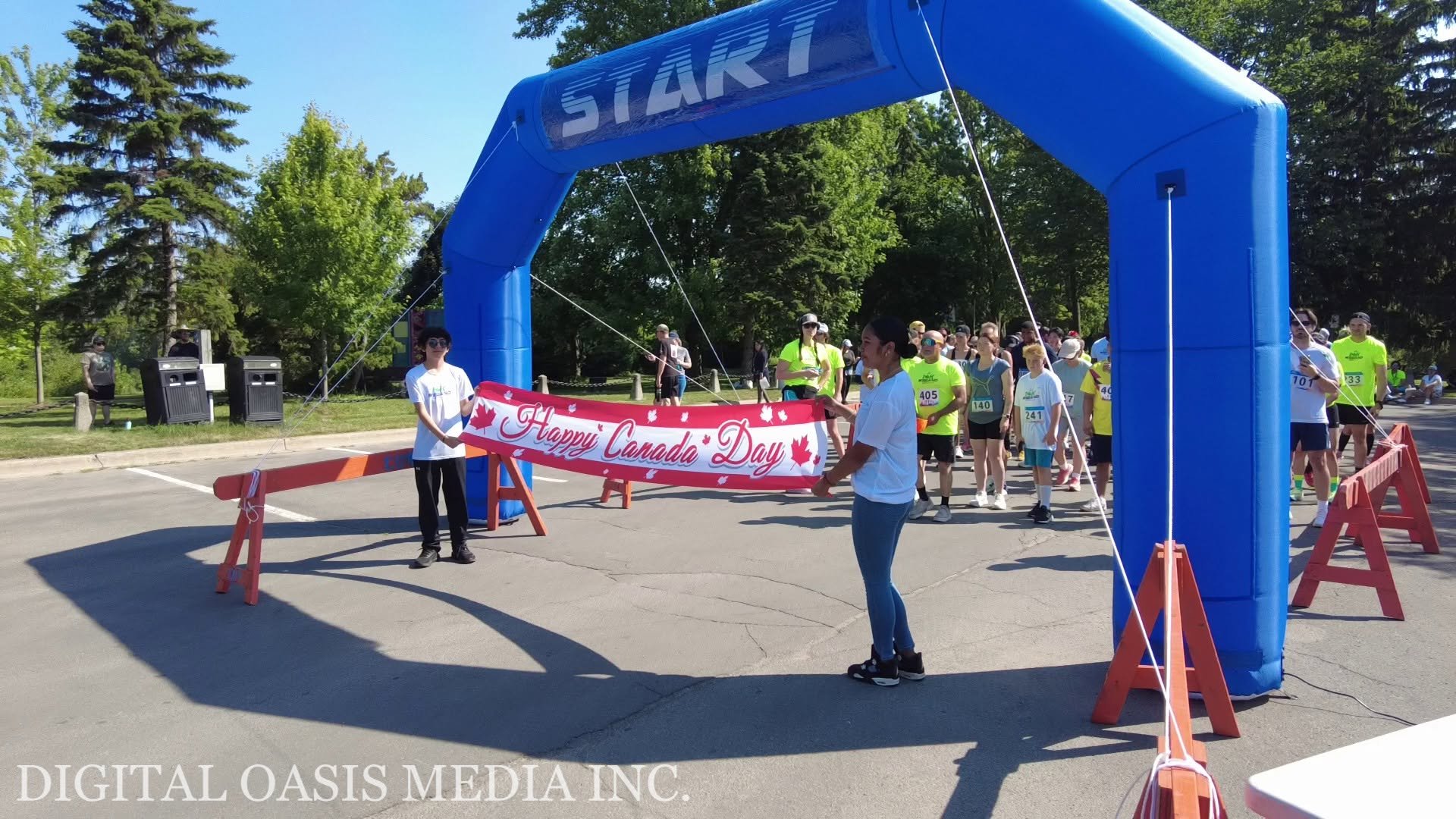Runners gather beneath a blue START arch while holding a Happy Canada Day banner.
