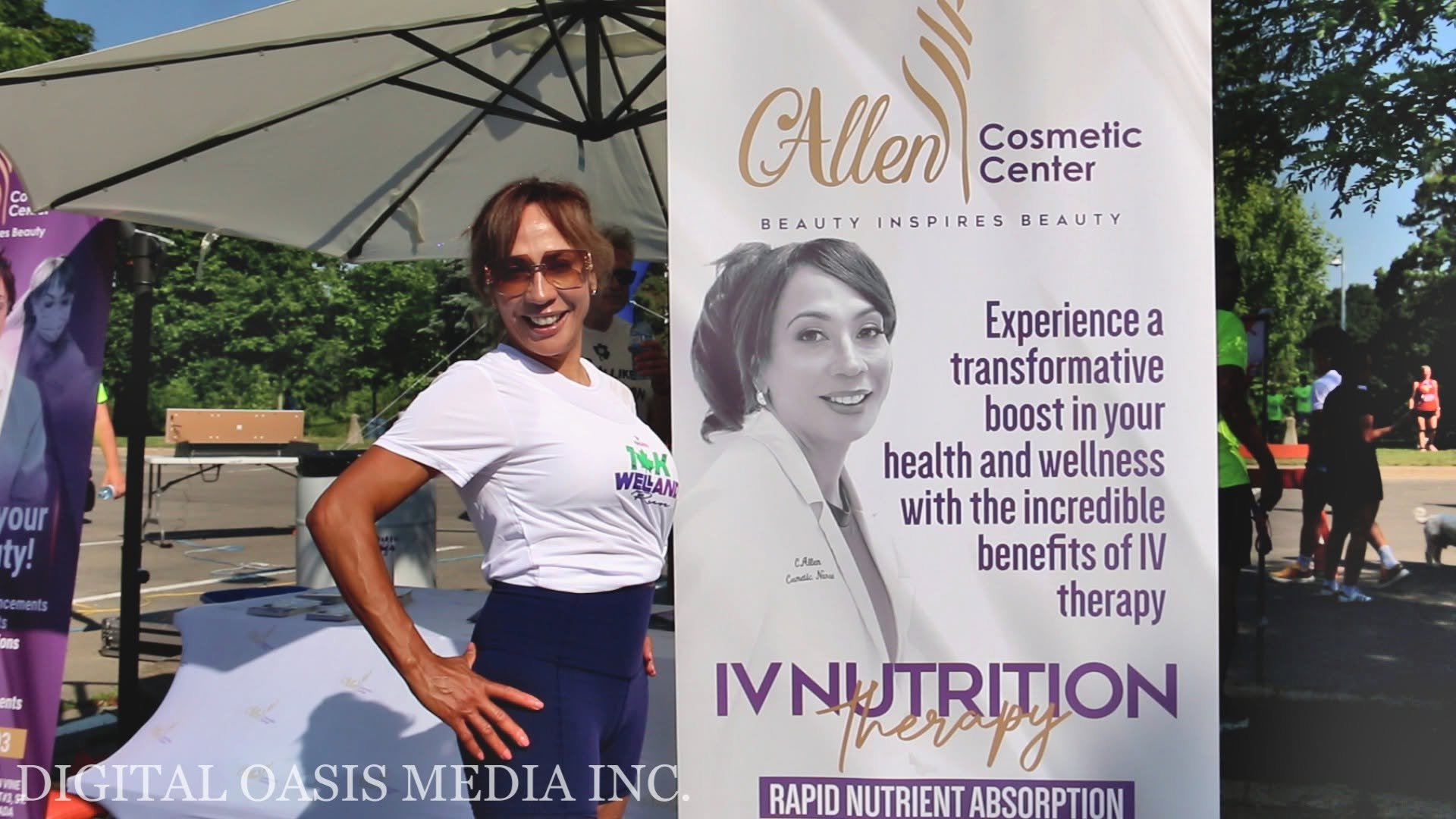 Woman poses beside an Allen Cosmetic Center IV nutrition therapy banner at an outdoor event.