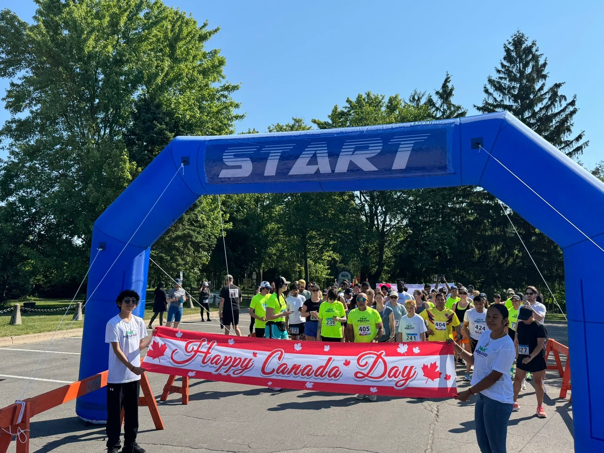 Runners gather beneath a blue “START” arch behind a “Happy Canada Day” maple-leaf banner.