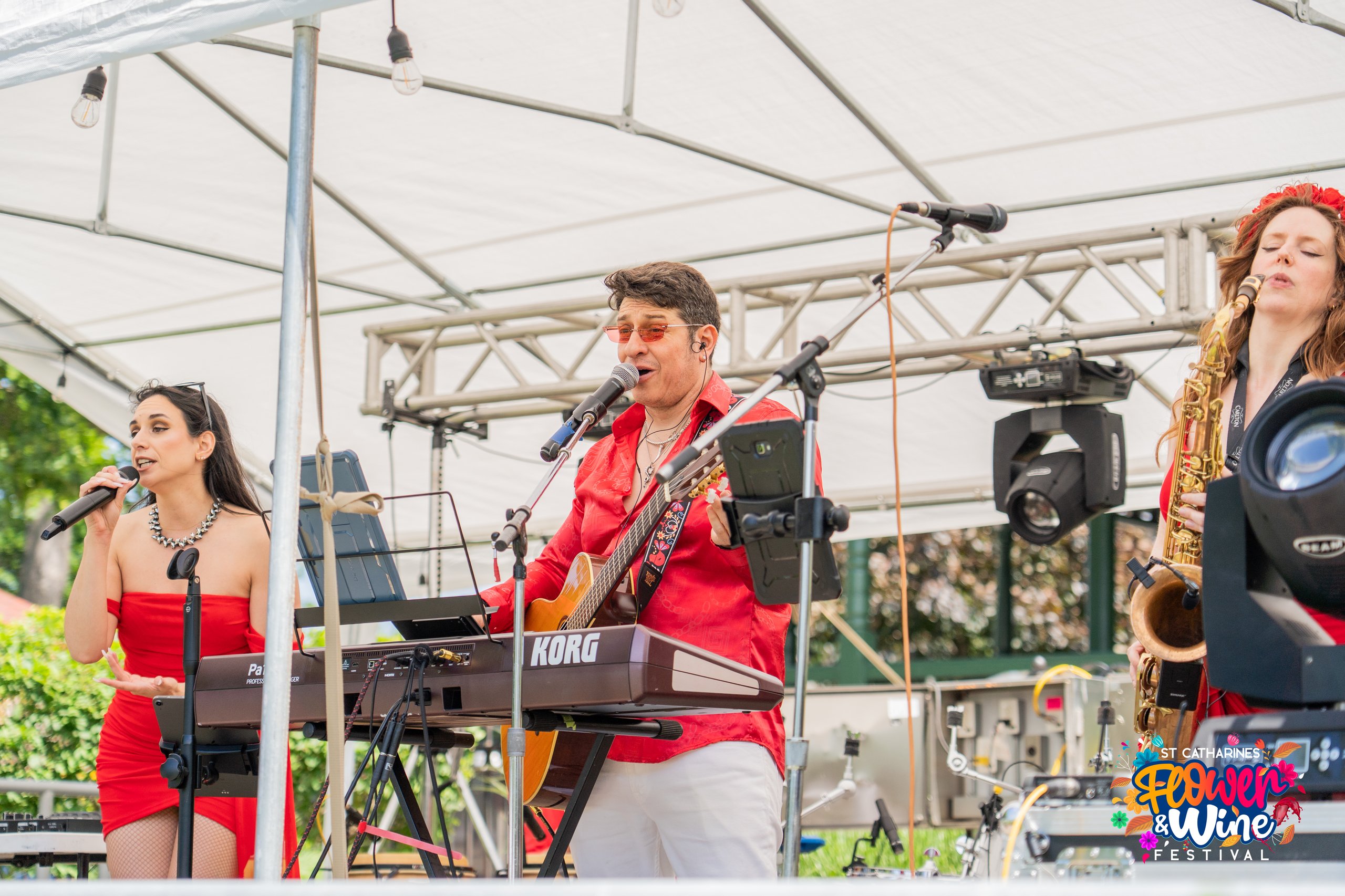 Musicians perform under a canopy, with saxophones, a guitarist, microphones, and a colorful St. Catharines festival logo.